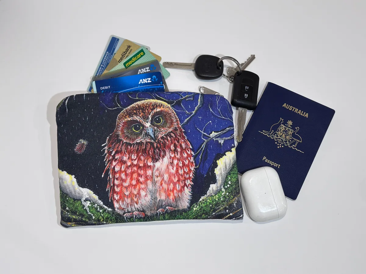 The boobook owl pouch beside keys, cards, a passport and earbuds, showing its size.
