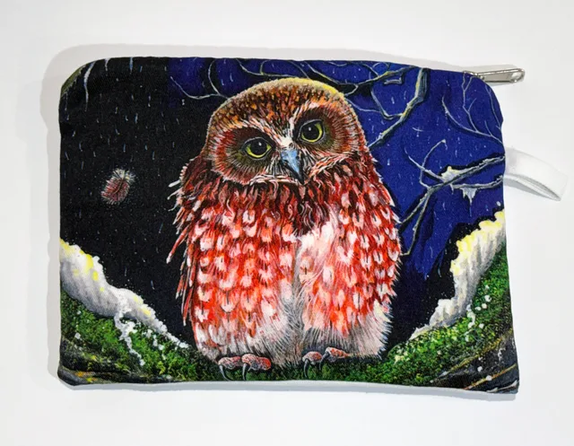 A zip-up cotton pouch printed with a small rusty-red boobook owl with large yellow-green eyes, perched on a mossy branch against a starry night sky of deep blue and black.