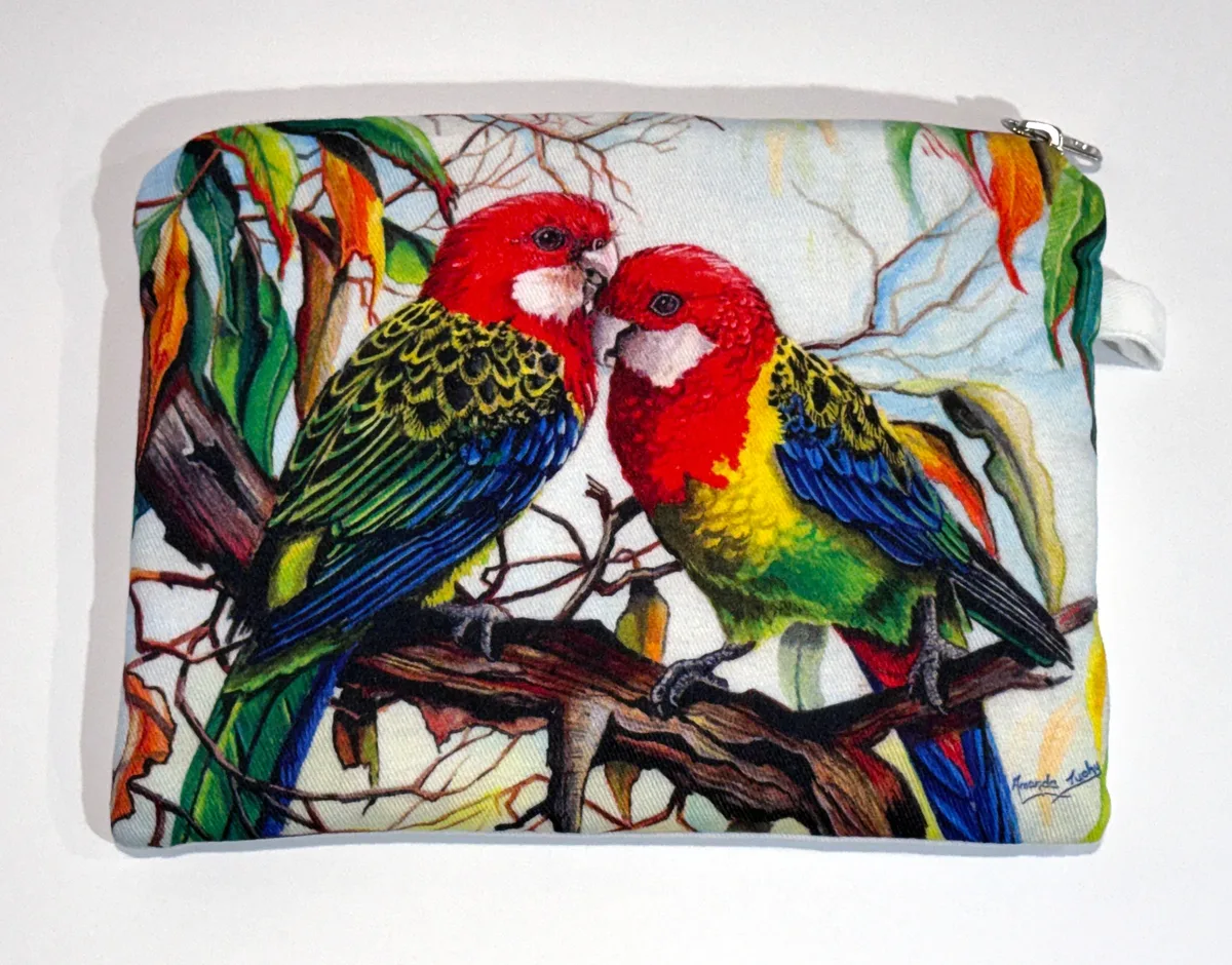 A zip-up cotton pouch printed with two eastern rosellas facing each other on a gum branch, their heads red with white cheeks, their backs scalloped black and yellow-green and their wings blue, among green and orange gum leaves.