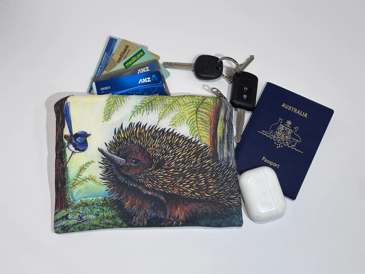 The echidna pouch beside keys, cards, a passport and earbuds, showing its size.