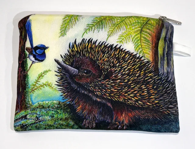A zip-up cotton pouch printed with an echidna with yellow and orange-tipped spines, facing a small wren in bright blue and black plumage that clings to a tree trunk on the left, among ferns and green moss.