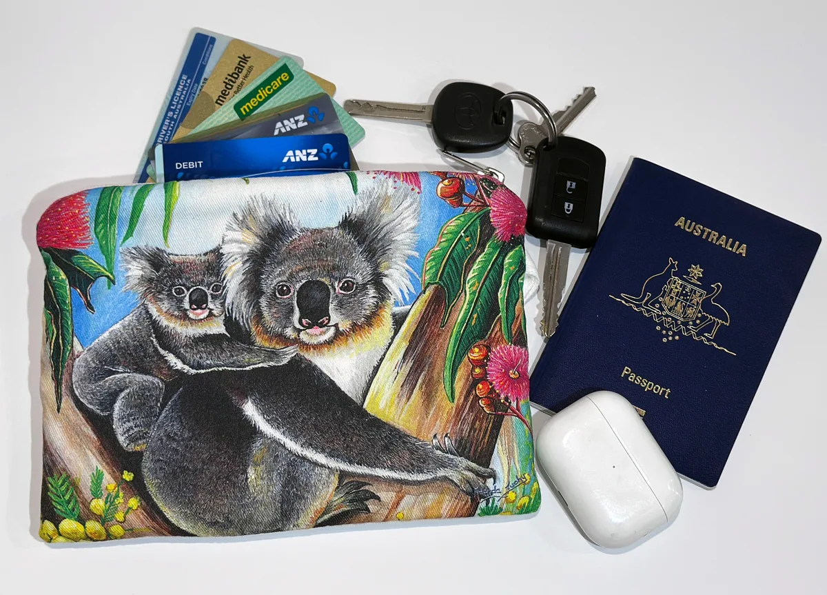 The koalas pouch beside keys, cards, a passport and earbuds, showing its size.