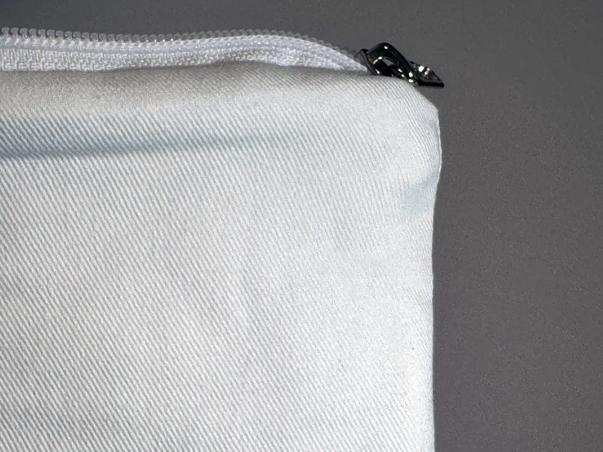 A close-up of a pouch’s white cotton twill fabric and zip, with the metal zip pull at the corner.