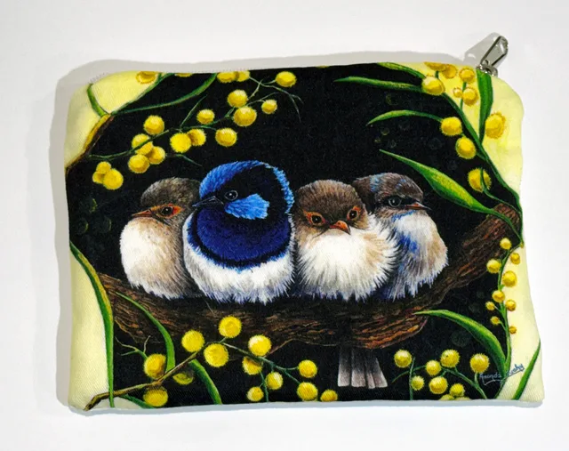 A zip-up cotton pouch printed with four small wrens huddled together on a branch, one bright blue and black and three soft brown and white, framed by golden wattle blossom against a dark background.